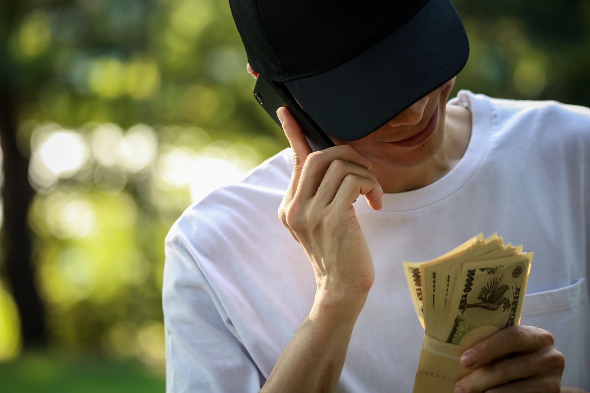 A young man talks on a cell phone while looking at an envelope filled with Japanese banknotes.