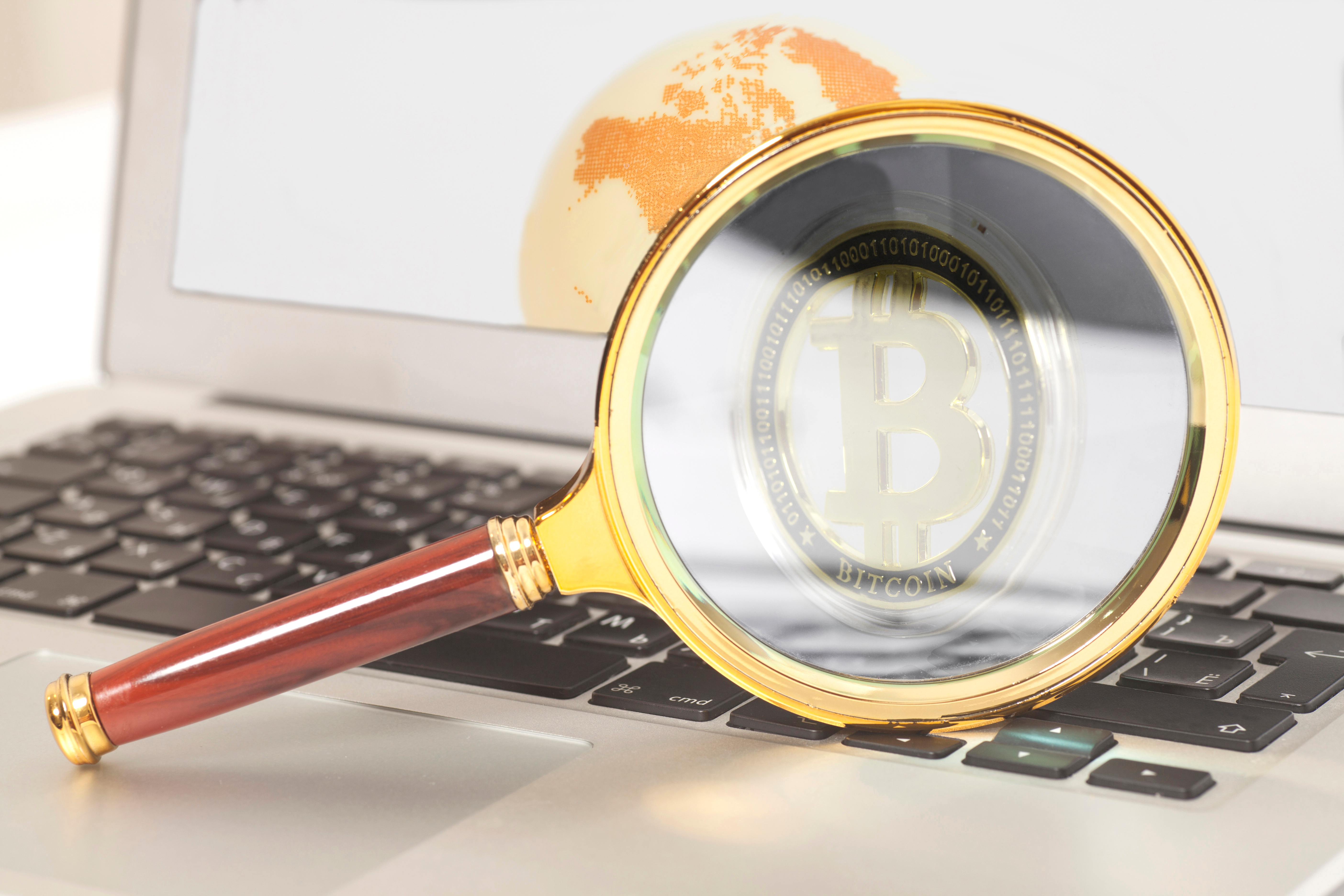 A magnifying glass focuses on a Bitcoin logo on a laptop PC&amp;amp;rsquo;s screen.
