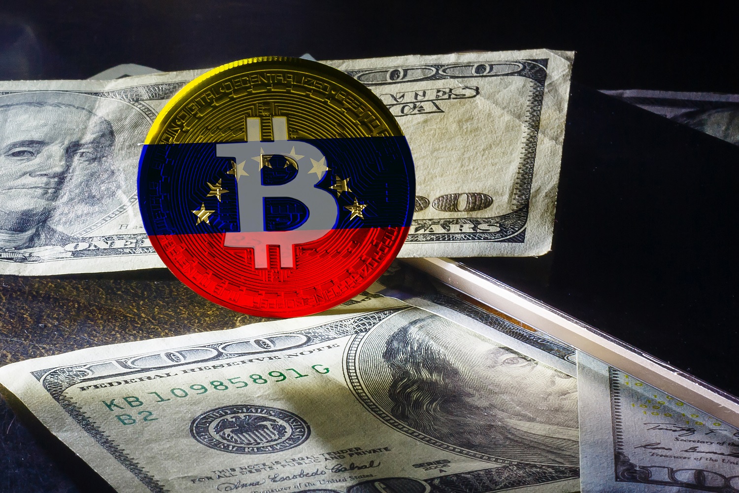 Bitcoin logosu ve Venezüella bayrağının renkleri ile süslenmiş bir jeton, birkaç 100 dolarlık banknotun yanında duruyor.