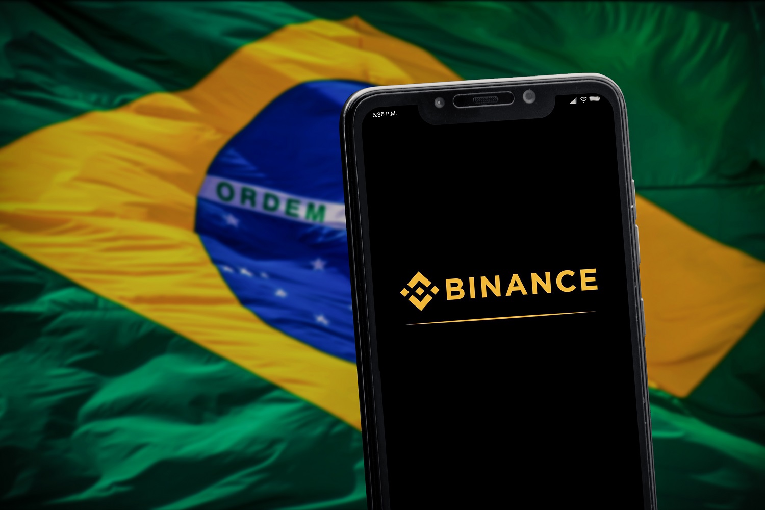 The Binance logo on a smartphone screen against a background of the Brazilian flag.