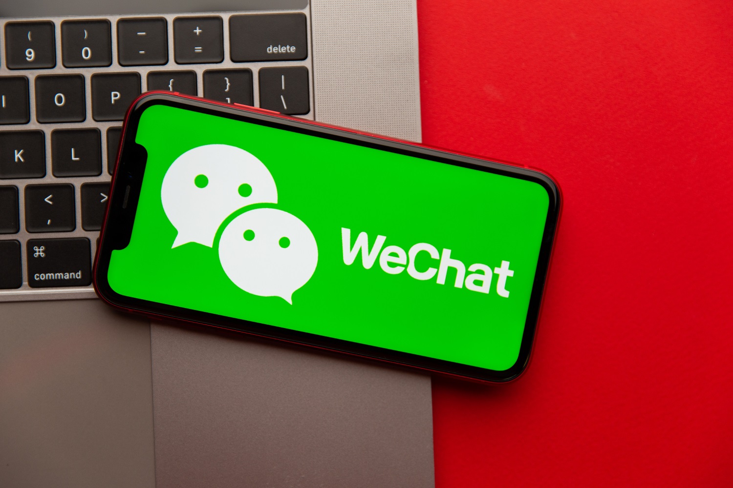 Arka planda dizüstü bilgisayar klavyesi bulunan bir akıllı telefonun ekranında çalışan WeChat mobil uygulaması.