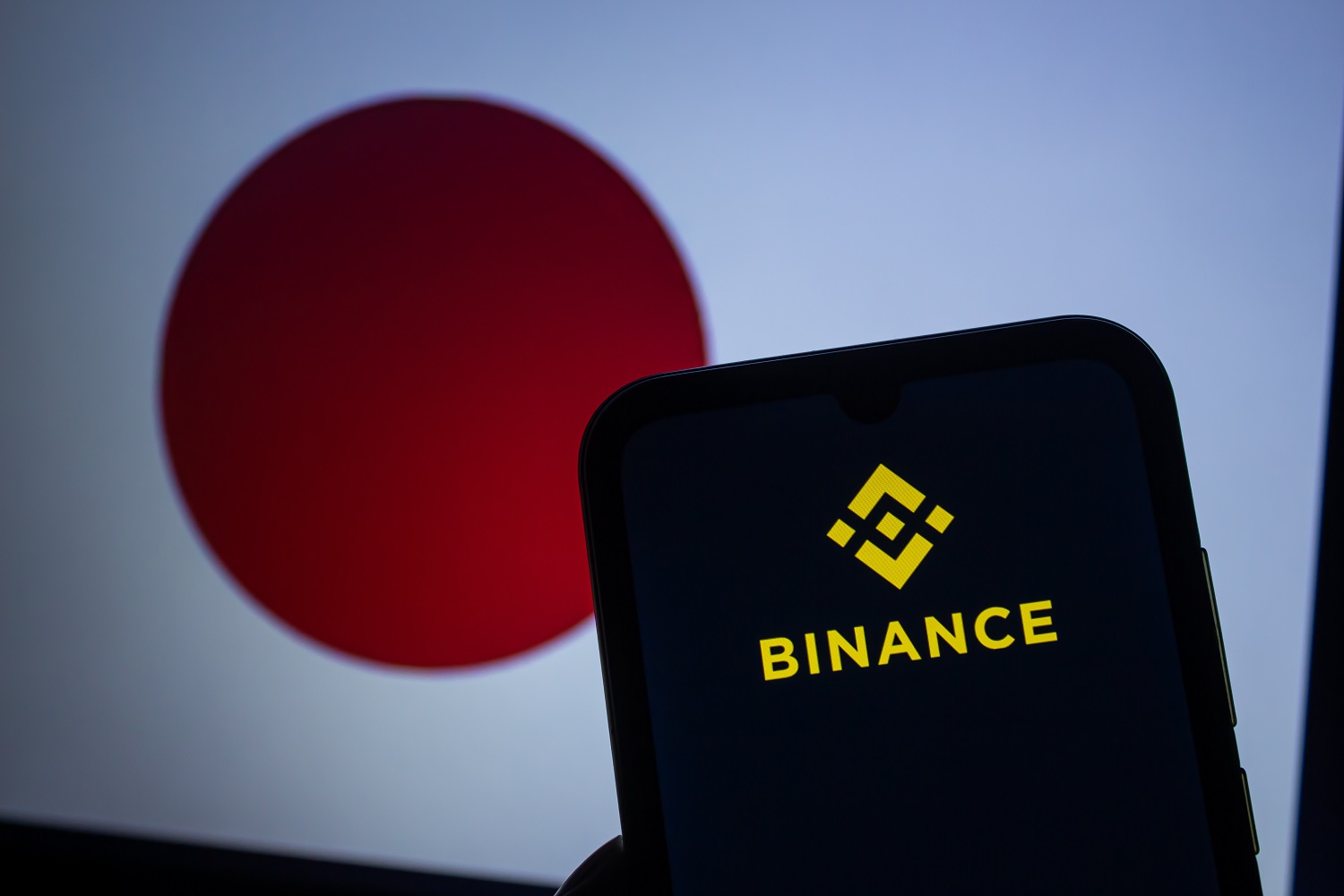 The Binance logo displayed on a smartphone screen against the backdrop of the flag of Japan.