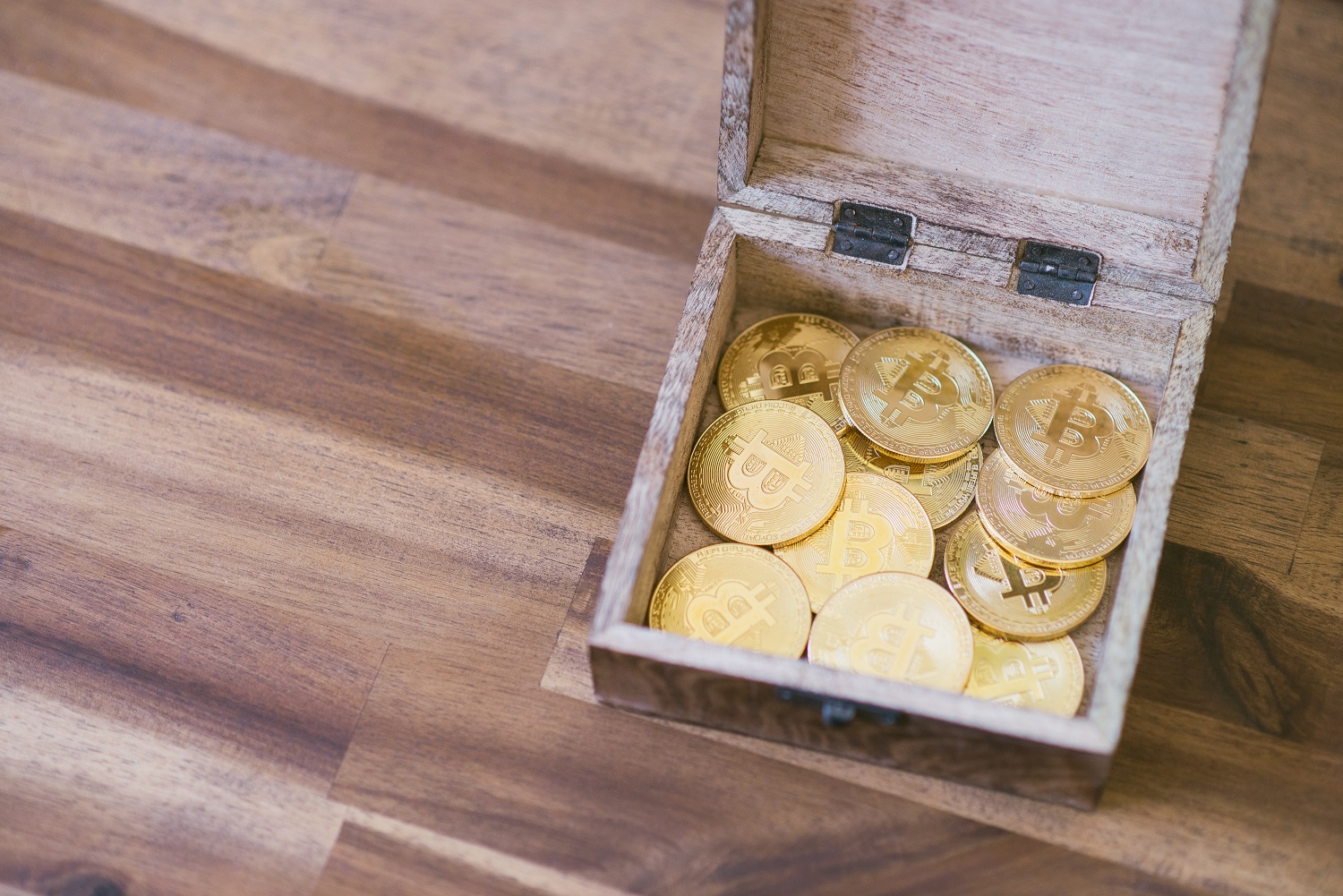Ahşap bir zemin veya masa üzerinde Bitcoin'i temsil etmeyi amaçlayan altın jetonlar içeren ahşap bir kutu.