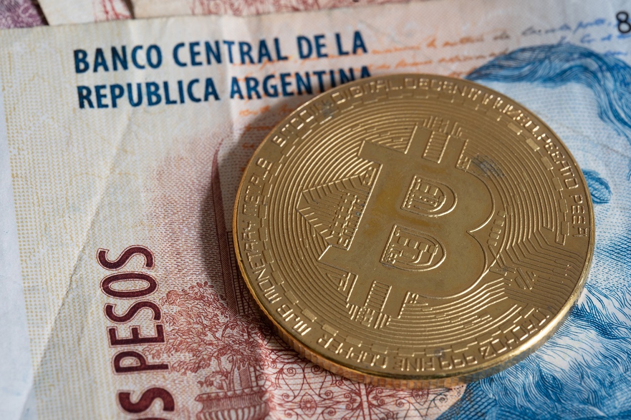 Bitcoin'i temsil eden metal bir madeni para, bir Arjantin banknotunun üzerinde duruyor.