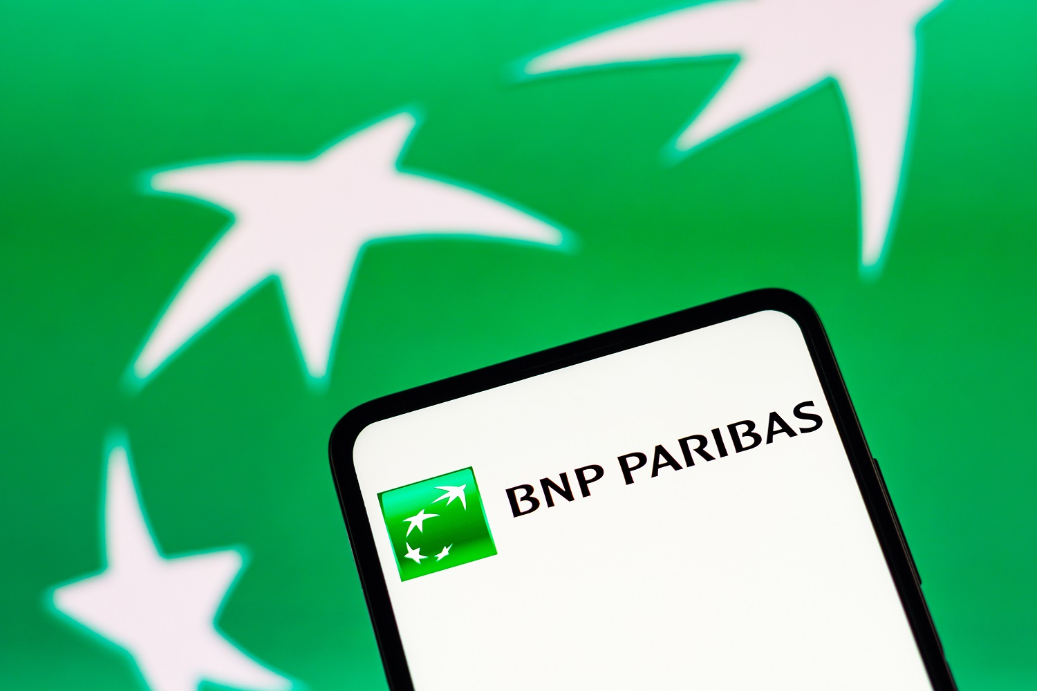 The BNP Paribas logo on a smartphone screen against the backdrop of a larger, green BNP Paribas logo background.