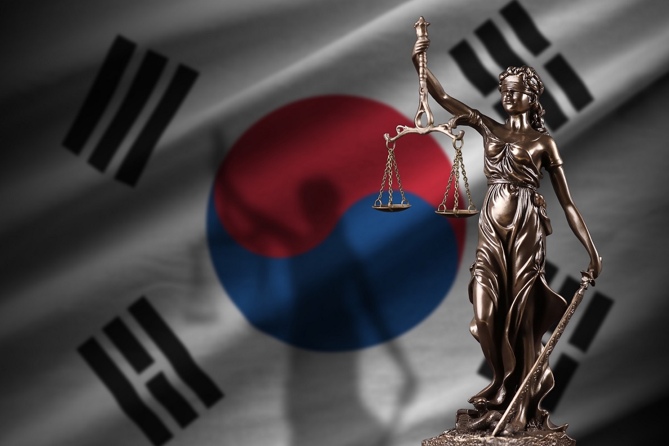 A statue of Lady Justice, blindfolded and holding scales and a sword, in front of a South Korean flag.