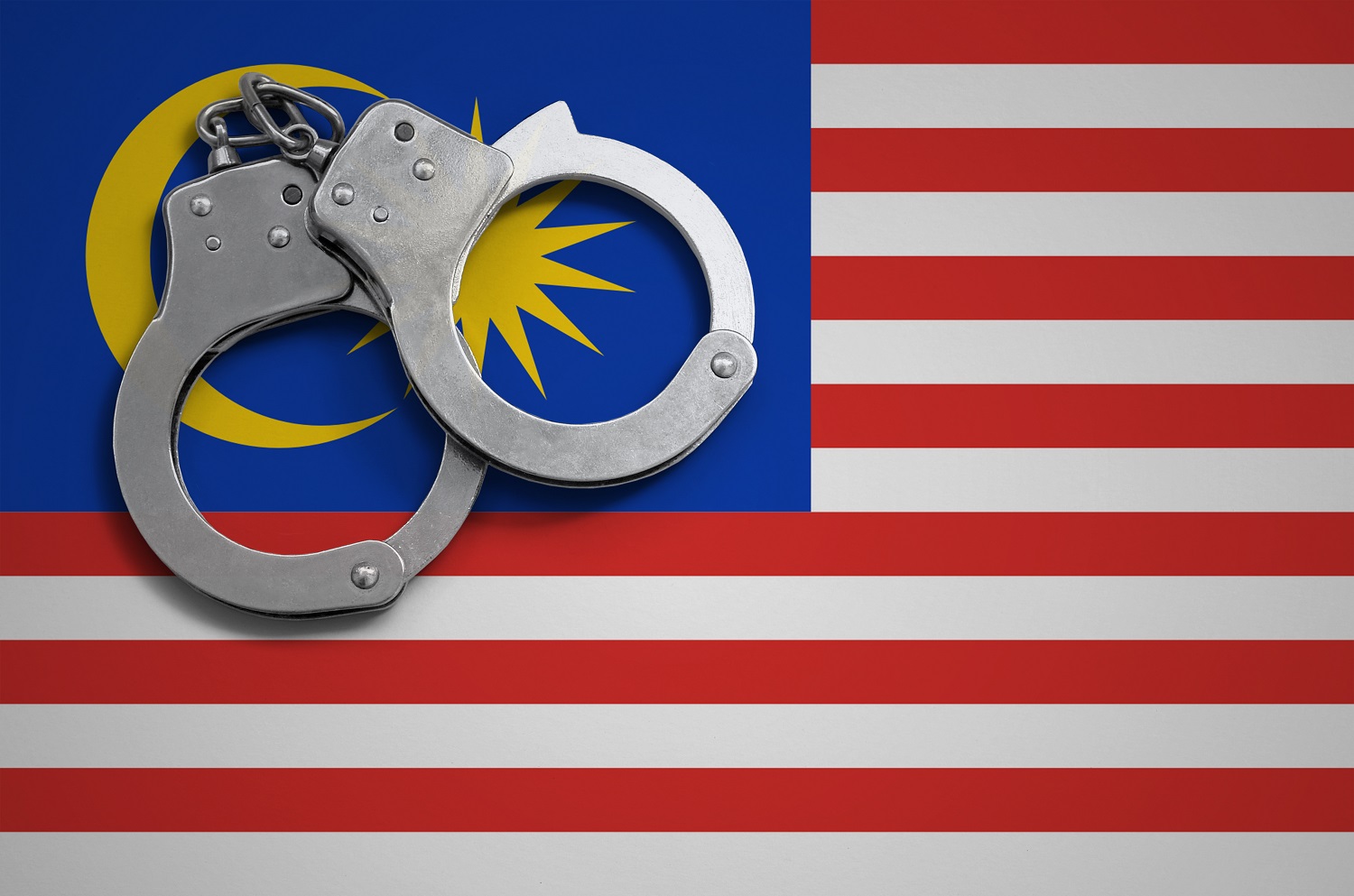 A pair of police handcuffs rests on the flag of Malaysia.