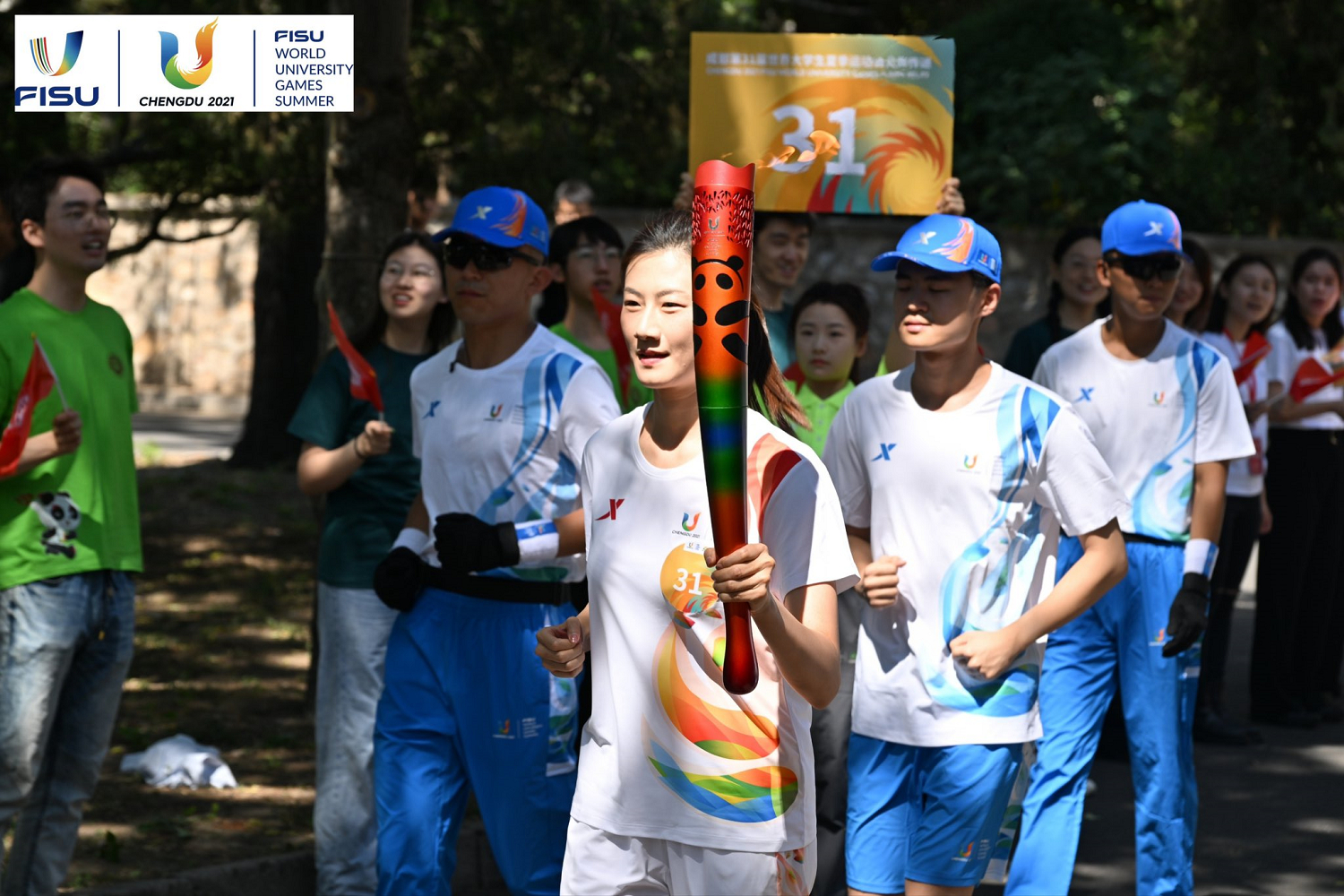   A Chinese student carries the Summer World University Games torch and runs down tree-lined a city road.